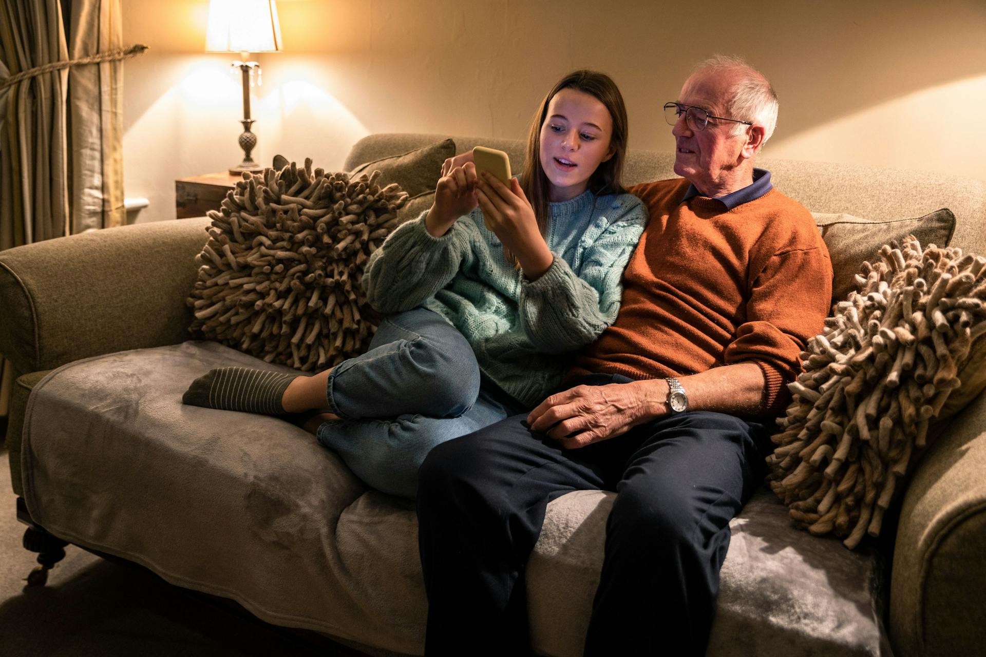 Ældre mand sidder med ung pige i en sofa mens de kigger på en telefon.