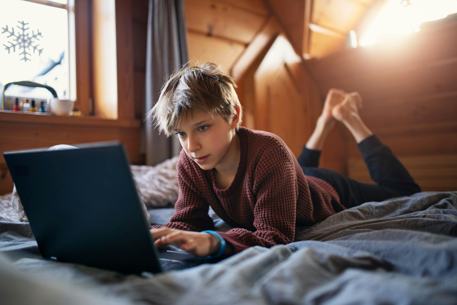 Ung dreng ligger i seng og kigger på computerskærm.