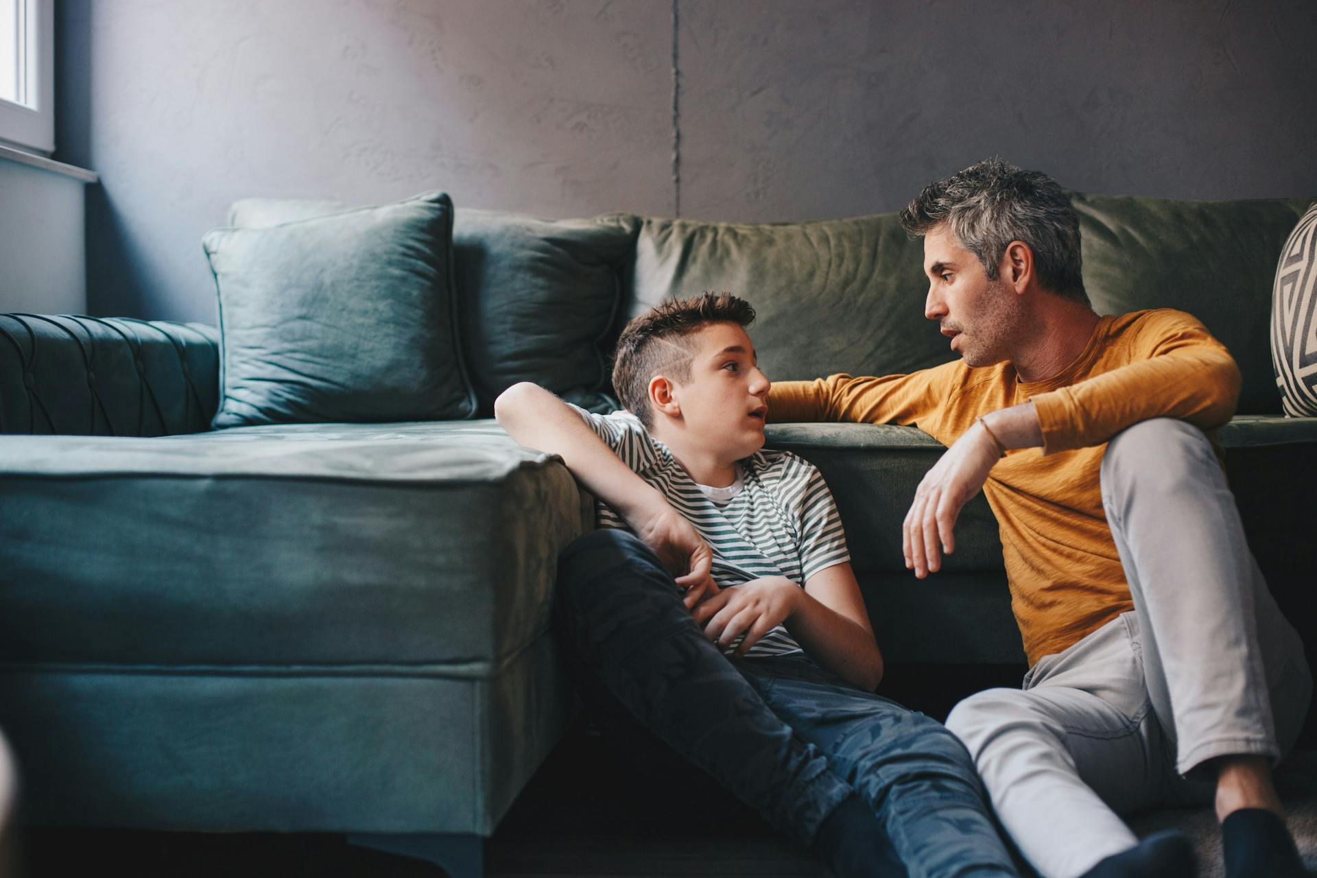 Mand og dreng sidder på gulvet foran sofa og har en alvorlig samtale.