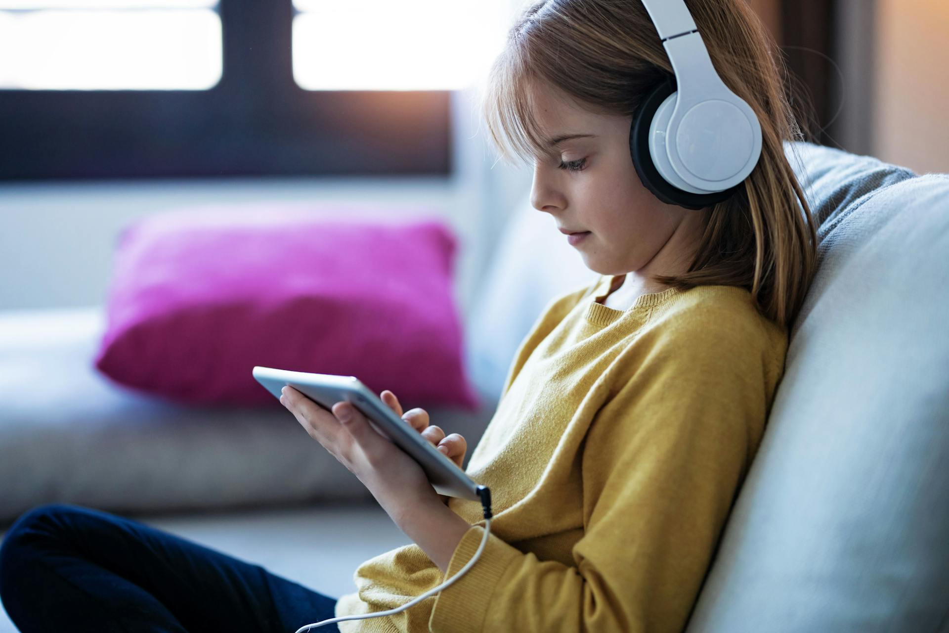 Ung pige sidder i en sofa med høretelefoner på og bruger en tablet.