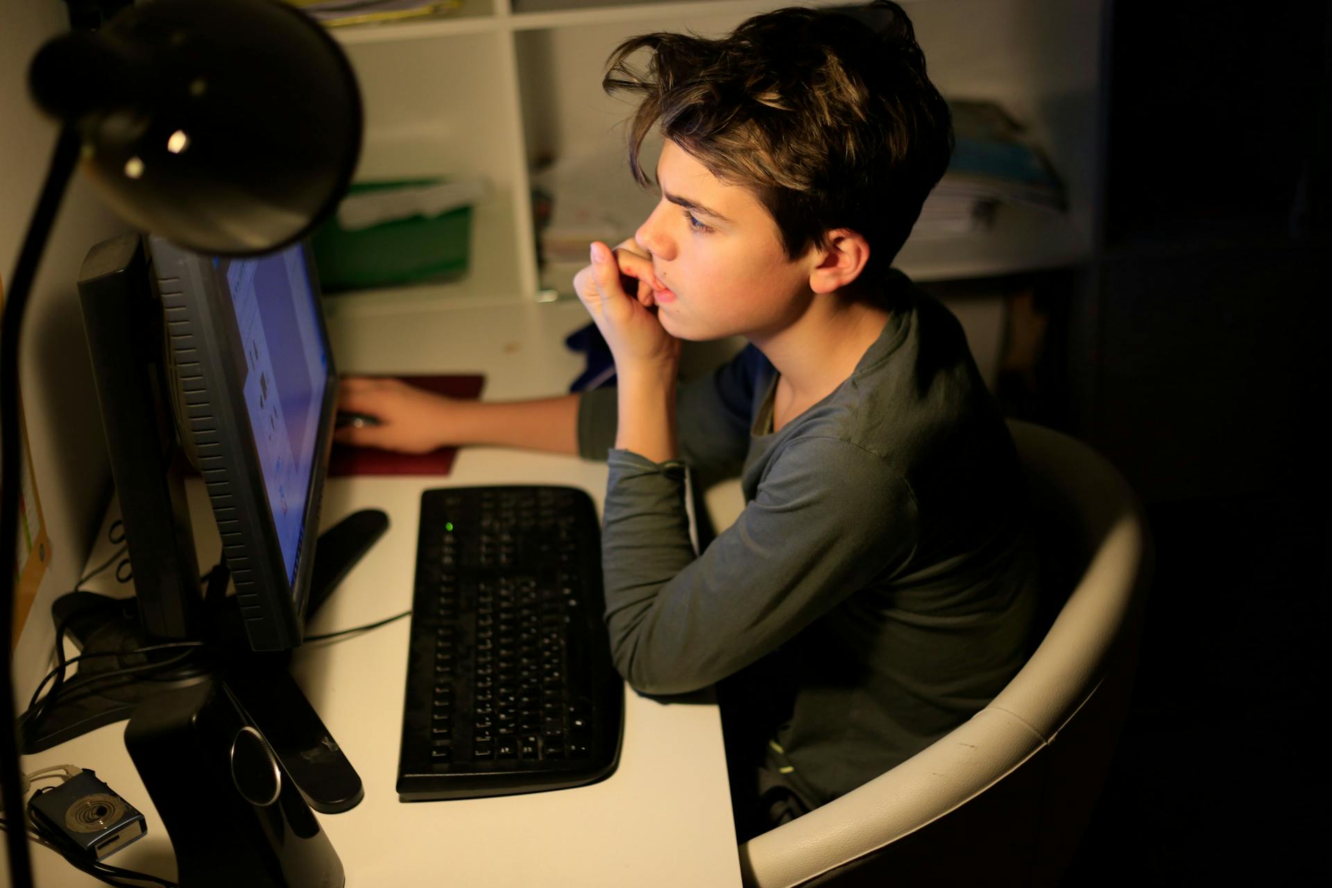 Dreng sidder ved skrivebord og kigger opslugt på computerskærm, mens han bider negle.