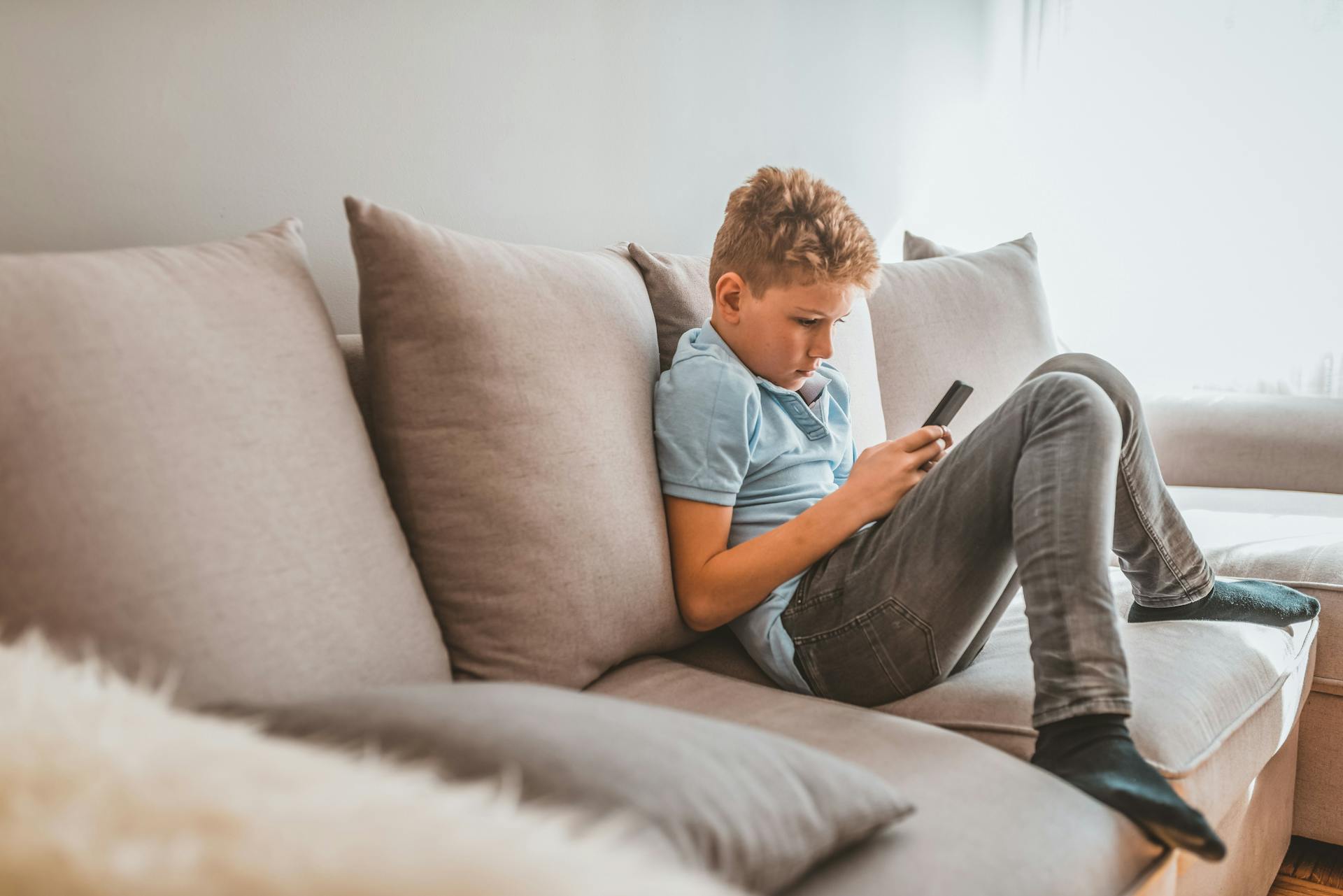 Dreng sidder på sofa med sin mobiltelefon