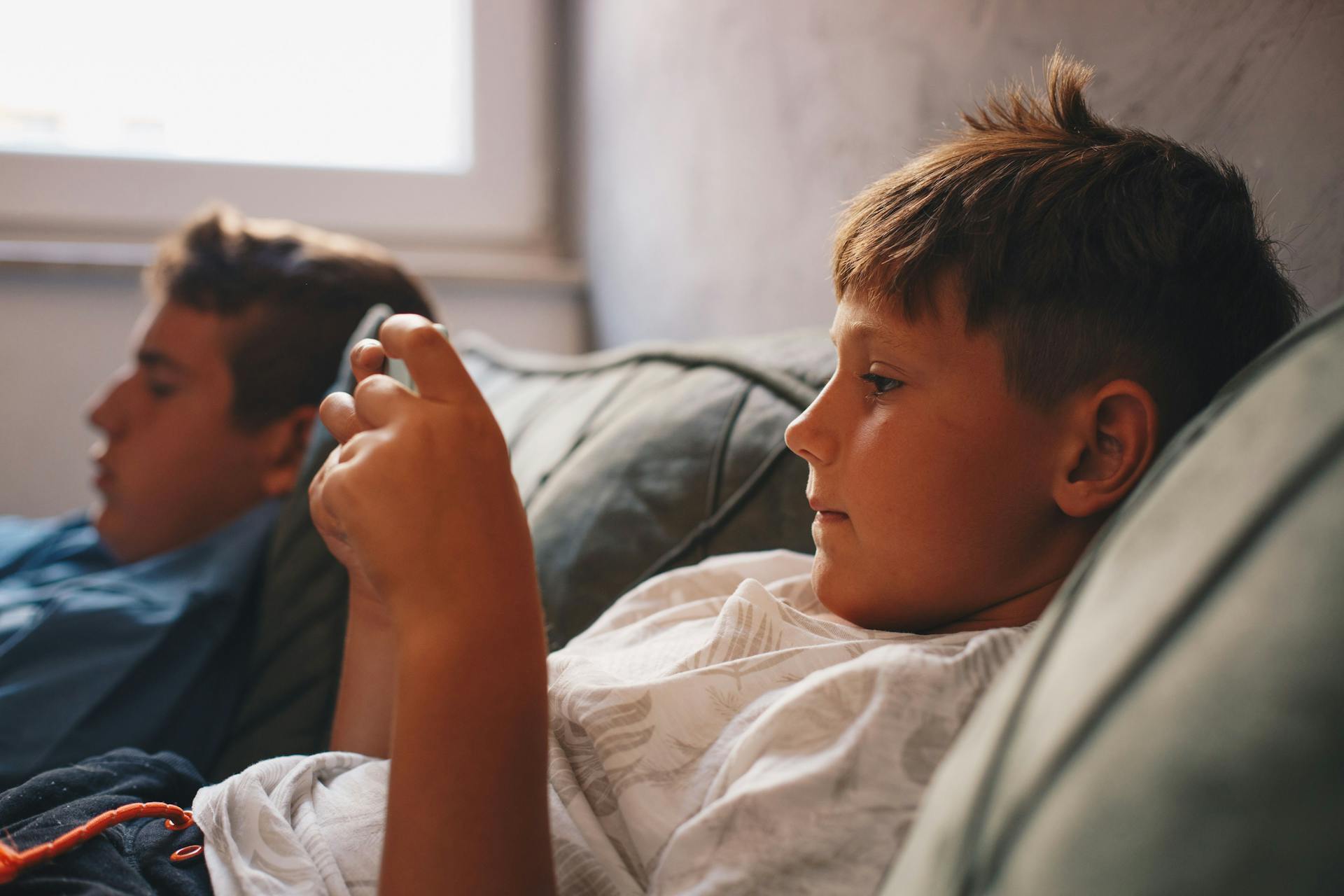 To drenge ligger i sofa og kigger på hver deres skærm.