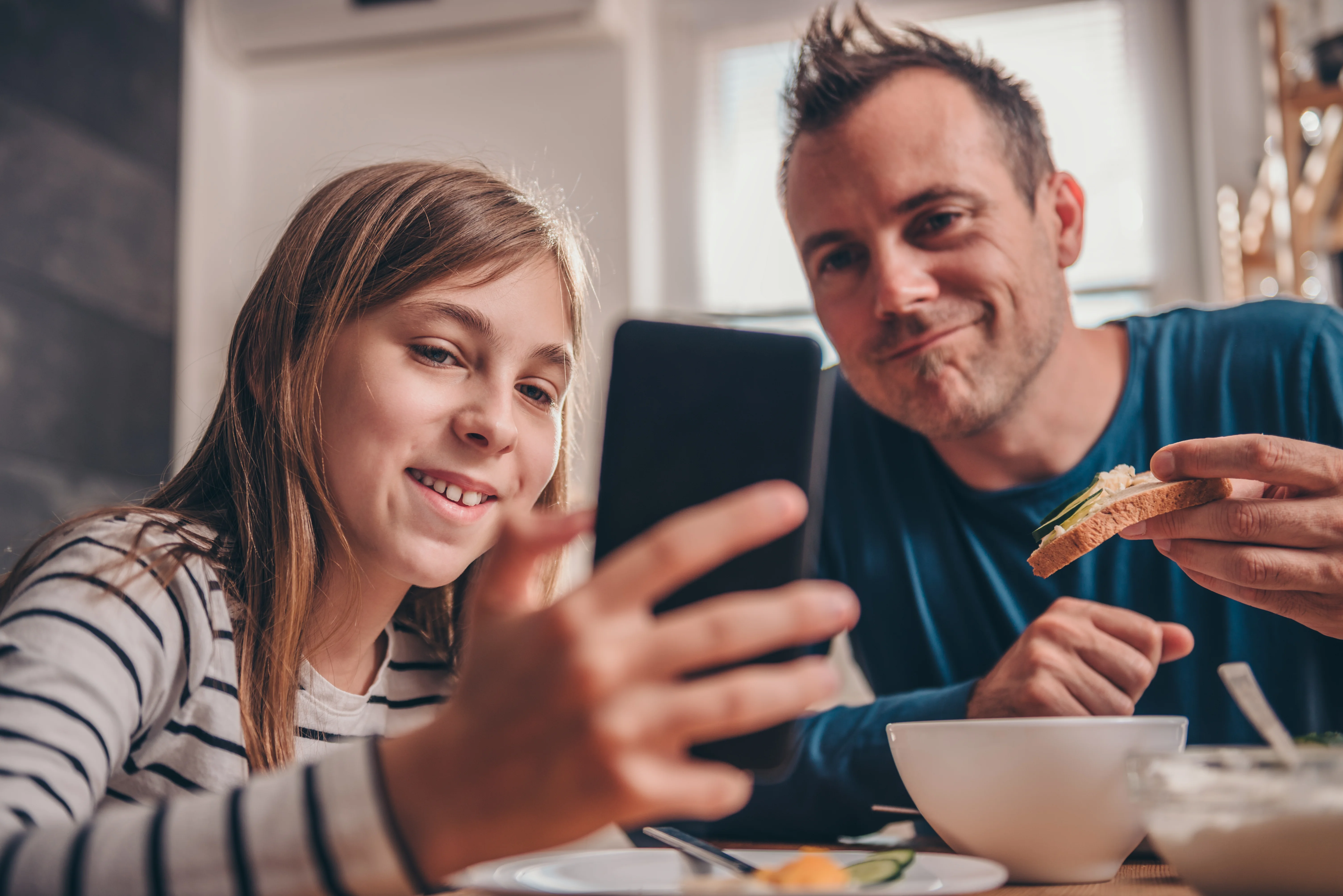 Far og barn kigger sammen på mobiltelefon og smiler
