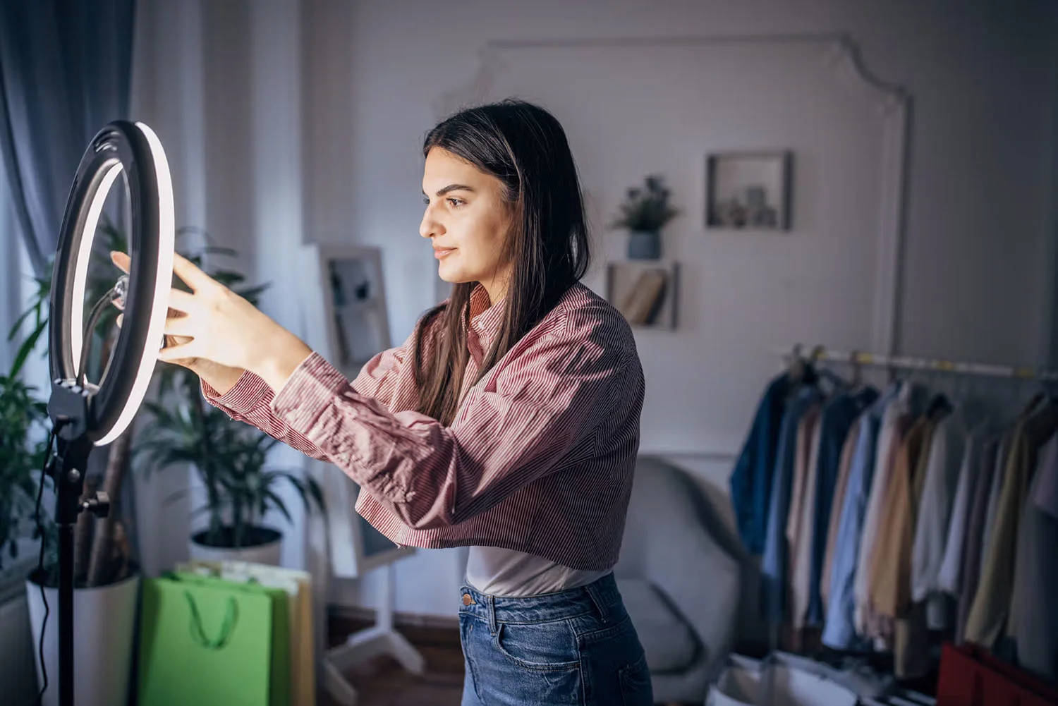 Ung kvinde står i sit soveværelse og sætter sin smartphone fast i en ring light.
